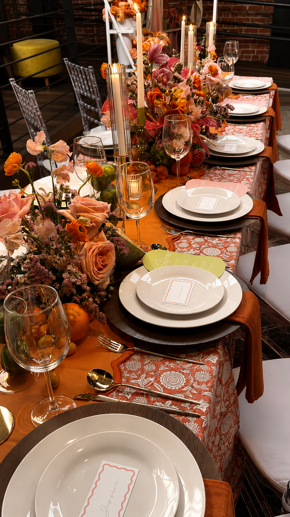 A candlelit banquet table dressed in coral linens, orange blooms, and tall taper candles